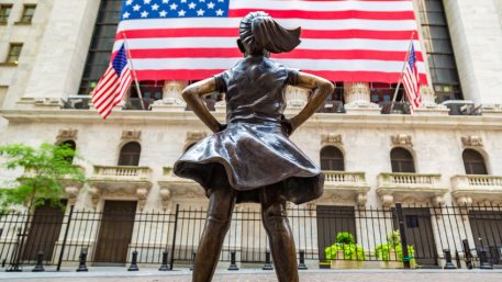 Fearless Girl Statue looking up at New York Stock Exchange building at Wall Street in Manhattan, New York City, USA