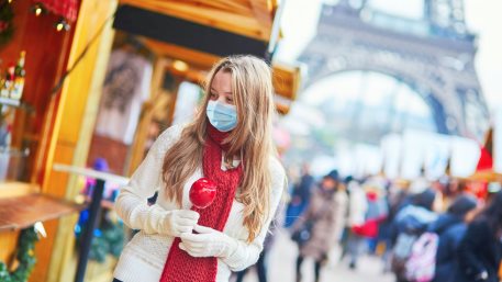 Girl wearing face mask with caramel apple on Parisian Christmas market