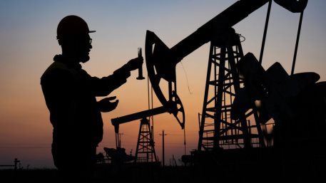 A chemical engineer taking a sample of crude oil against the background of oil pumps